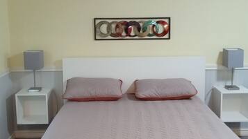 Una cama bien hecha con cubrecama acolchado, dos mesitas de noche con lámparas y una obra de arte en la pared sobre la cama.