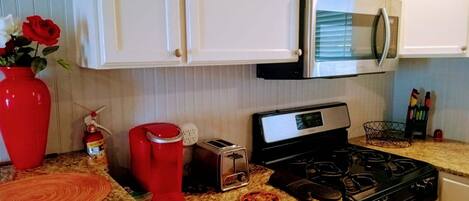 Una cocina con armarios blancos, microondas, estufa, tostadora y cafetera roja.