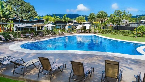 A swimming pool with lounge chairs and umbrellas, surrounded by greenery and buildings. - Macaw House with private pool in Arenas Herradura (Playa Herradura)