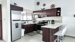 A modern kitchen with dark wood cabinets, stainless steel appliances, and a white countertop. - Macaw House with private pool in Arenas Herradura (Playa Herradura)