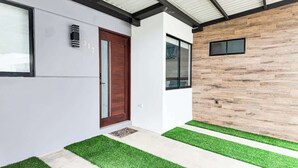 A modern house with a white exterior, a wooden door, and a brick wall. - Macaw House with private pool in Arenas Herradura (Playa Herradura)