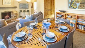 Un coin repas avec une table en bois dressée pour quatre personnes, entourée d’étagères et d’une cheminée.