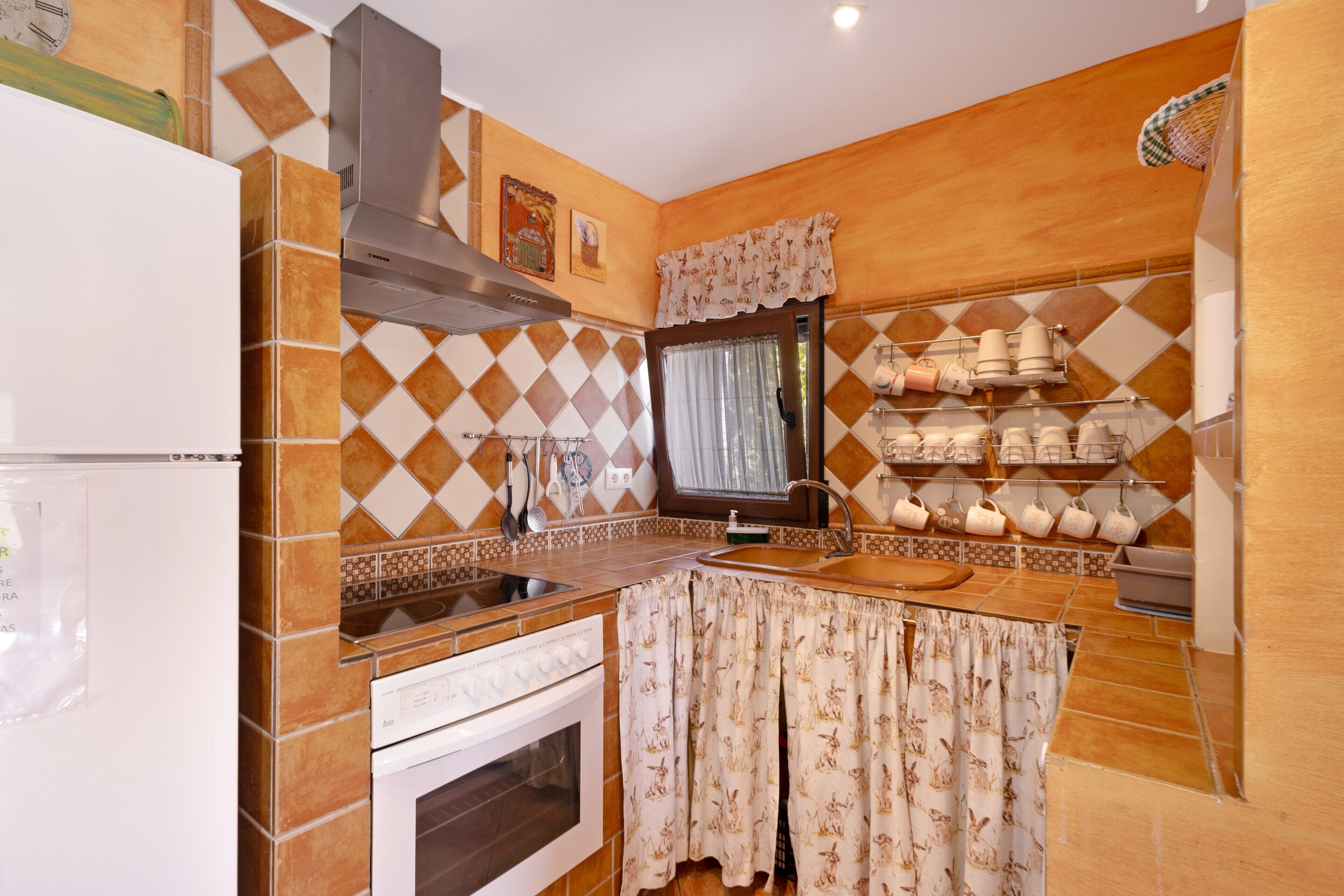 A kitchen with a stove, oven, sink, and a window with curtains.