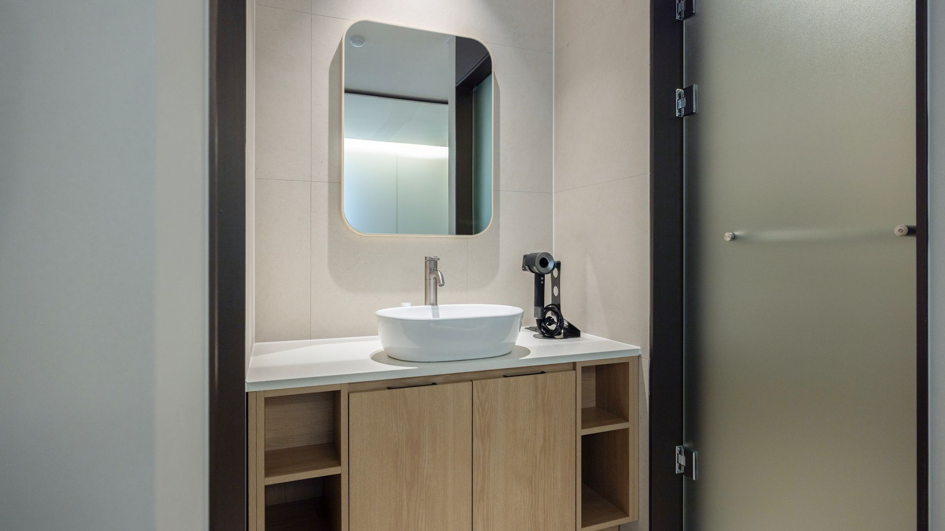 A modern bathroom with a white sink, a mirror, and a wooden vanity.