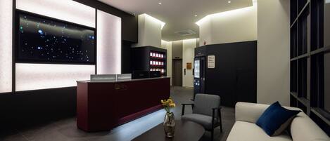 A modern lobby with a reception desk, seating area, and a large digital display.