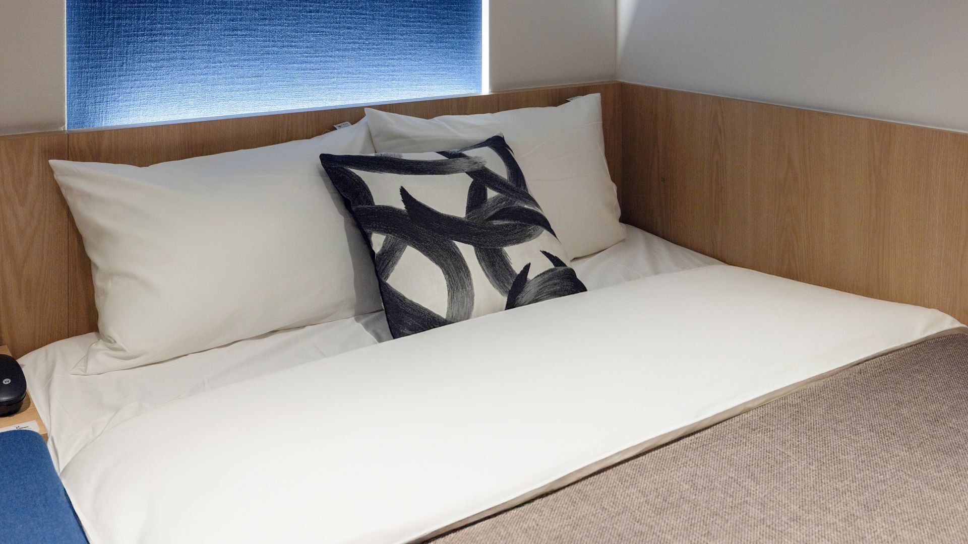 A neatly made bed with white bedding and a single black and white patterned pillow.