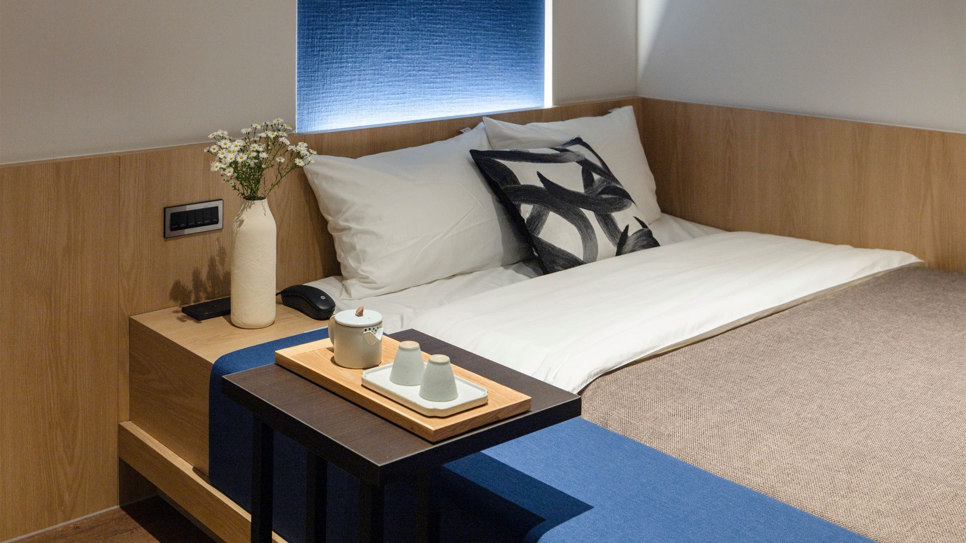 Habitación de hotel ordenada con cama, mesita de noche y una ventana pequeña.