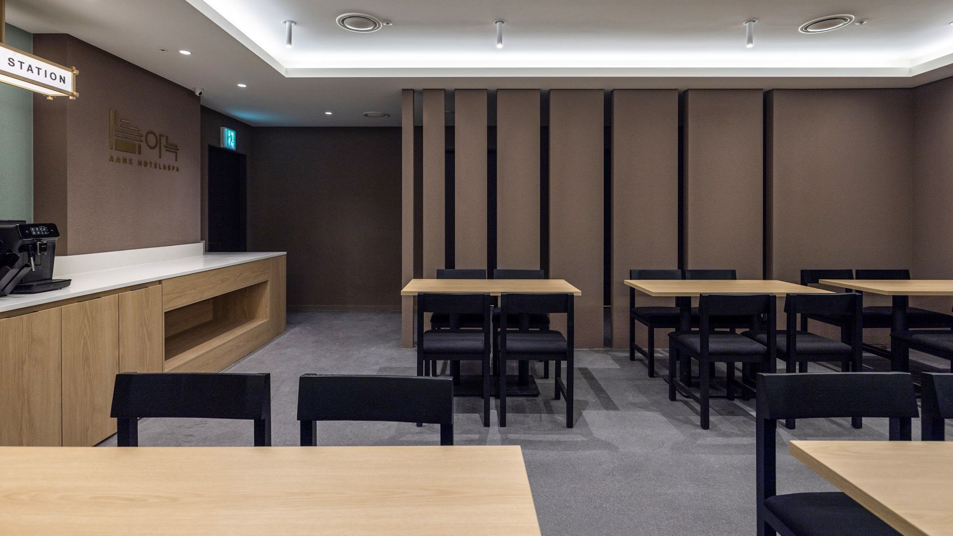A hotel reception area with a wooden counter, a coffee machine, and several tables and chairs.