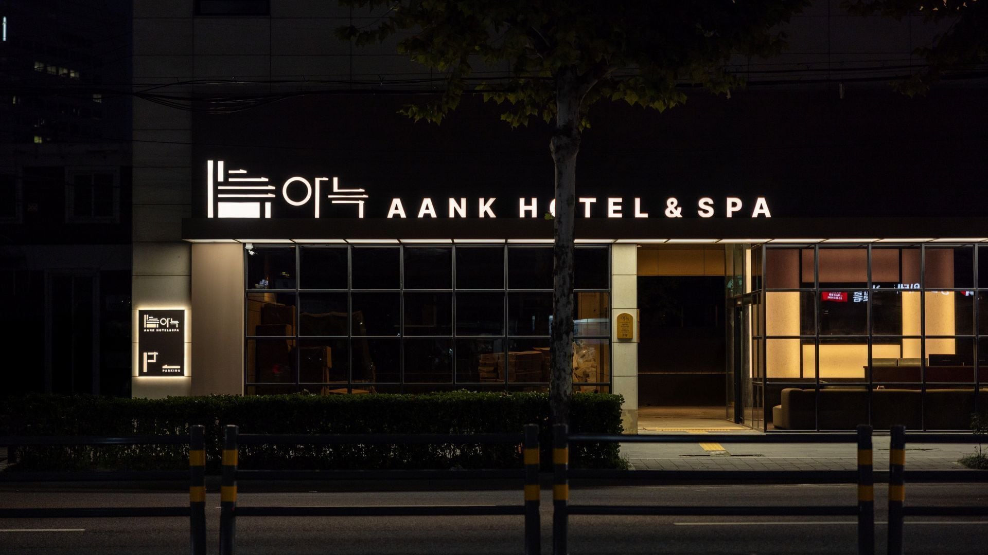 Un hotel con fachada moderna, señalización iluminada y un letrero de estacionamiento visible.