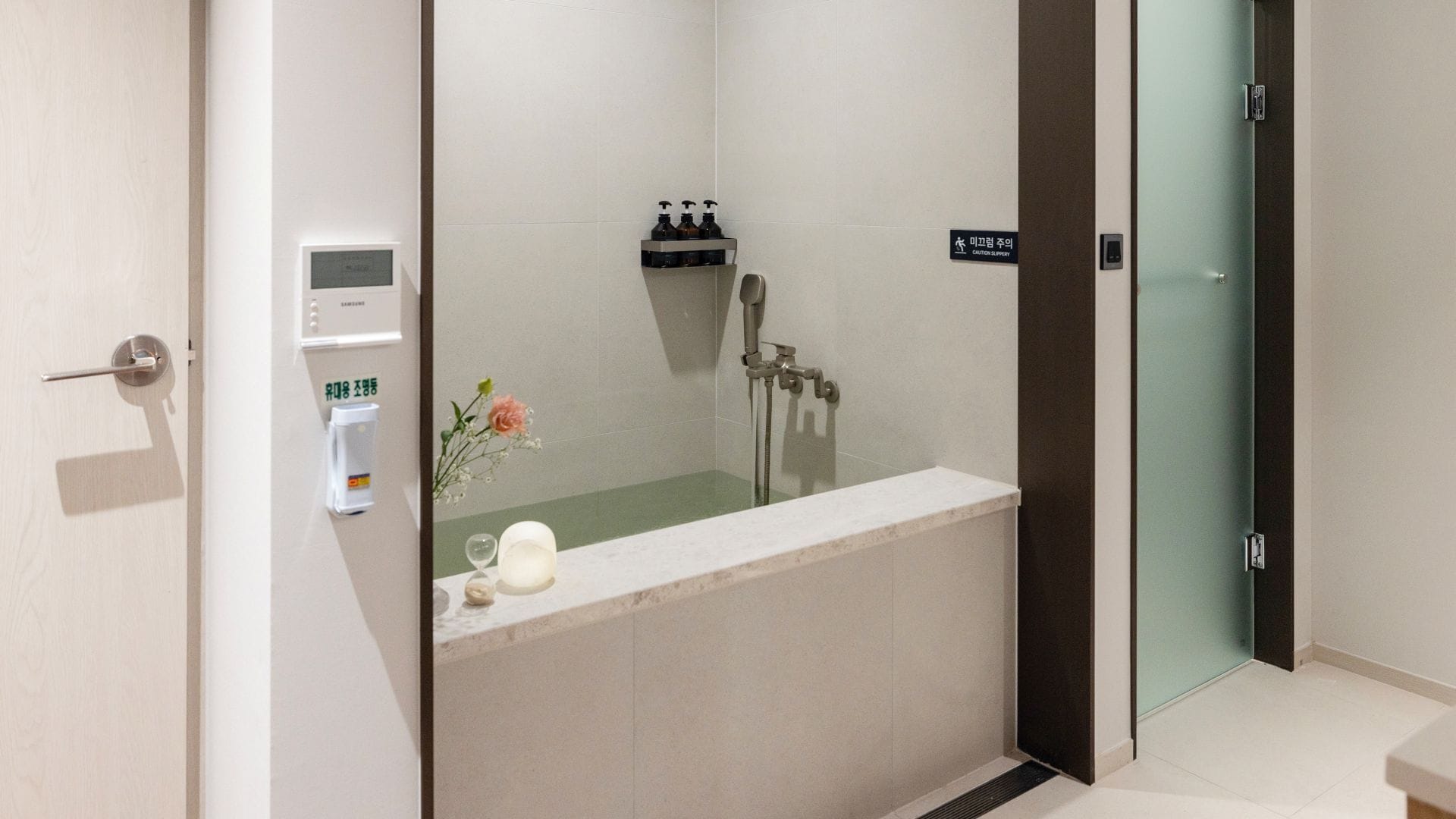 A modern bathroom with a bathtub, a shower, and a toilet. There is a hand sanitizer dispenser and a small flower arrangement on the counter.