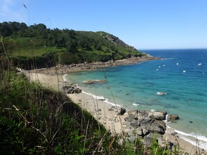 A coastal landscape with a rocky beach, clear turquoise waters, and a green hillside. - Holiday Home 'Entre Terre Et Mer' with Private Terrace, Private Garden and Wi-Fi (Locquirec)