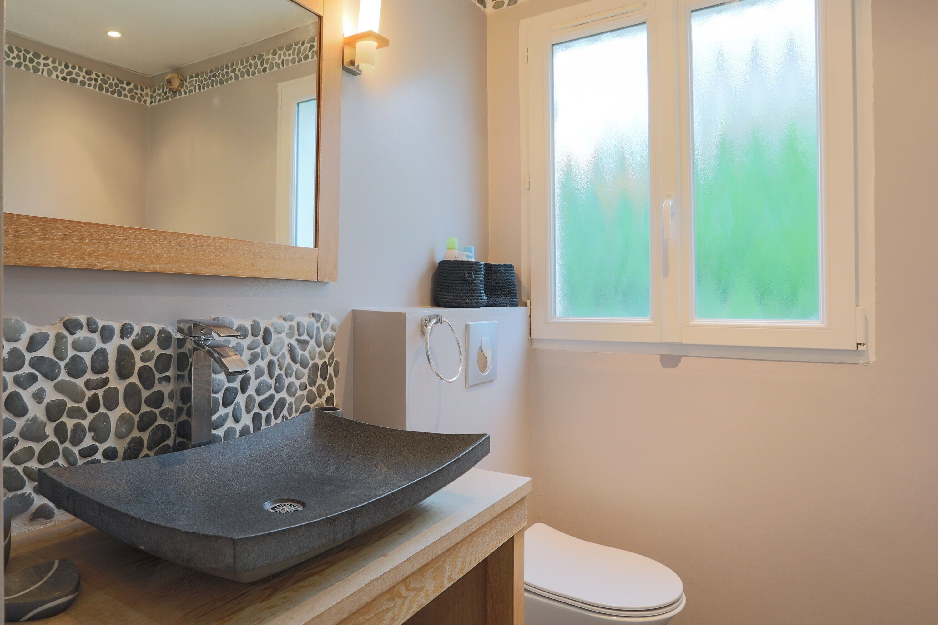 Une salle de bain avec un lavabo en pierre, un miroir, une fenêtre et des toilettes.