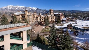 A multi-story hotel with a ski lift and snow-covered ground, surrounded by mountains.