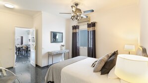 A hotel room with a bed, a desk, a chair, a ceiling fan, and a window with curtains.