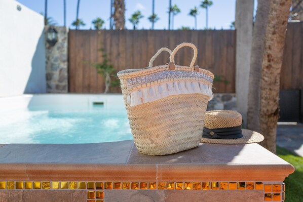 A woven basket and a straw hat on a stone ledge by a pool.