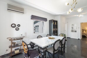 Un espace repas comprenant une table en marbre, des chaises noires et blanches, un buffet en métal et un lustre.