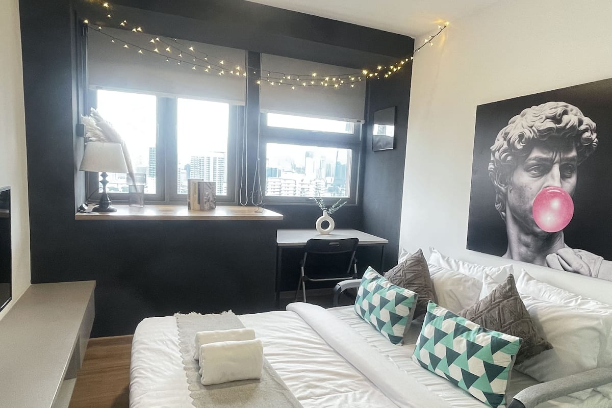 A modern bedroom with a bed, pillows, a desk, and a city view.