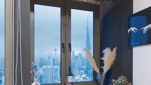 A room with a large window overlooking a cityscape, a wooden table with a wine glass, a vase with pampas grass, and a framed artwork on the wall. - Riveria Premium Kuala Lumpur, Roam (Kuala Lumpur)