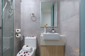 Un bagno moderno con box doccia in vetro, un water con asciugamano e petali di rosa, un lavabo con specchio e porta carta igienica.