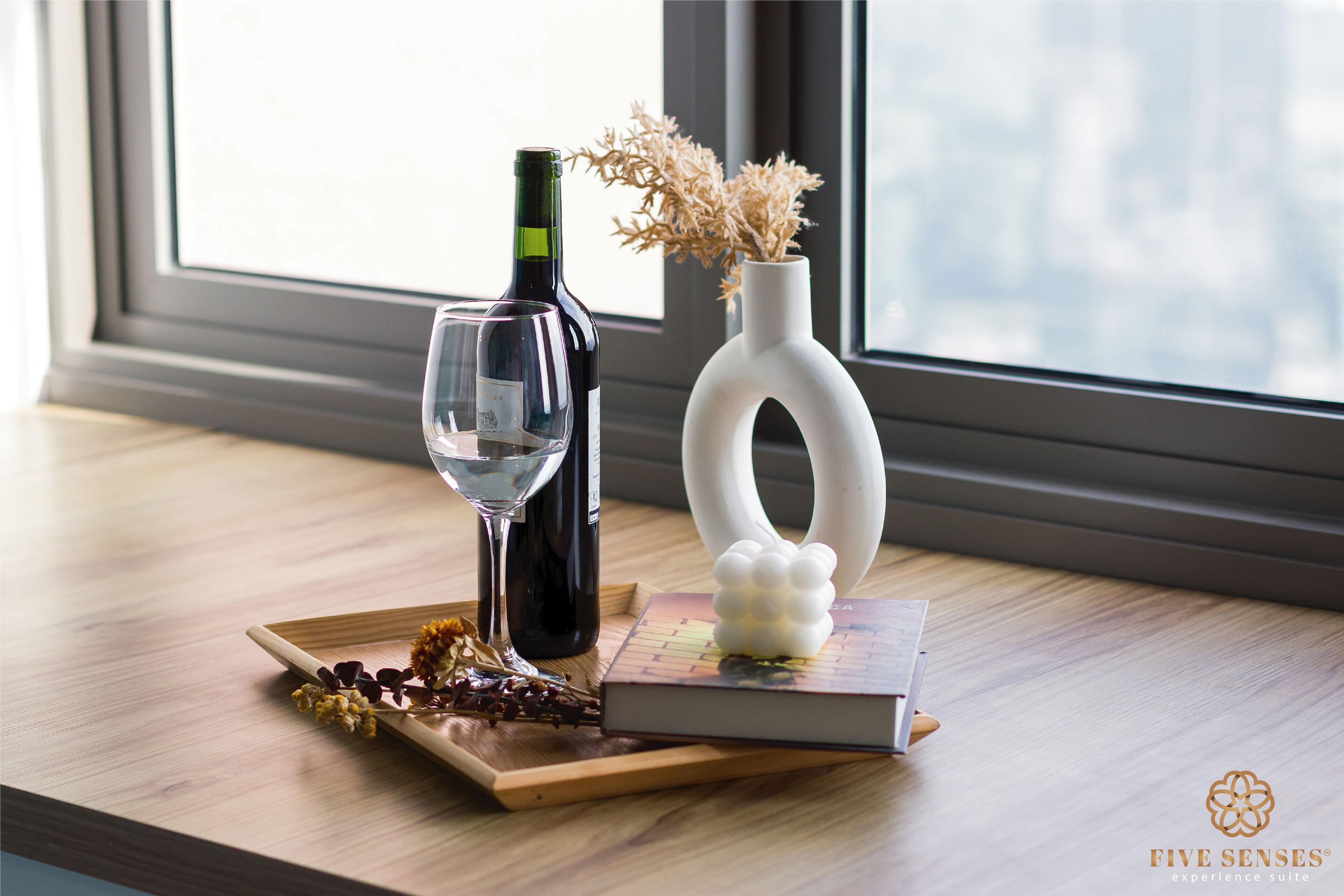 Une table en bois avec une bouteille de vin, un verre à vin, des fleurs séchées et un livre.