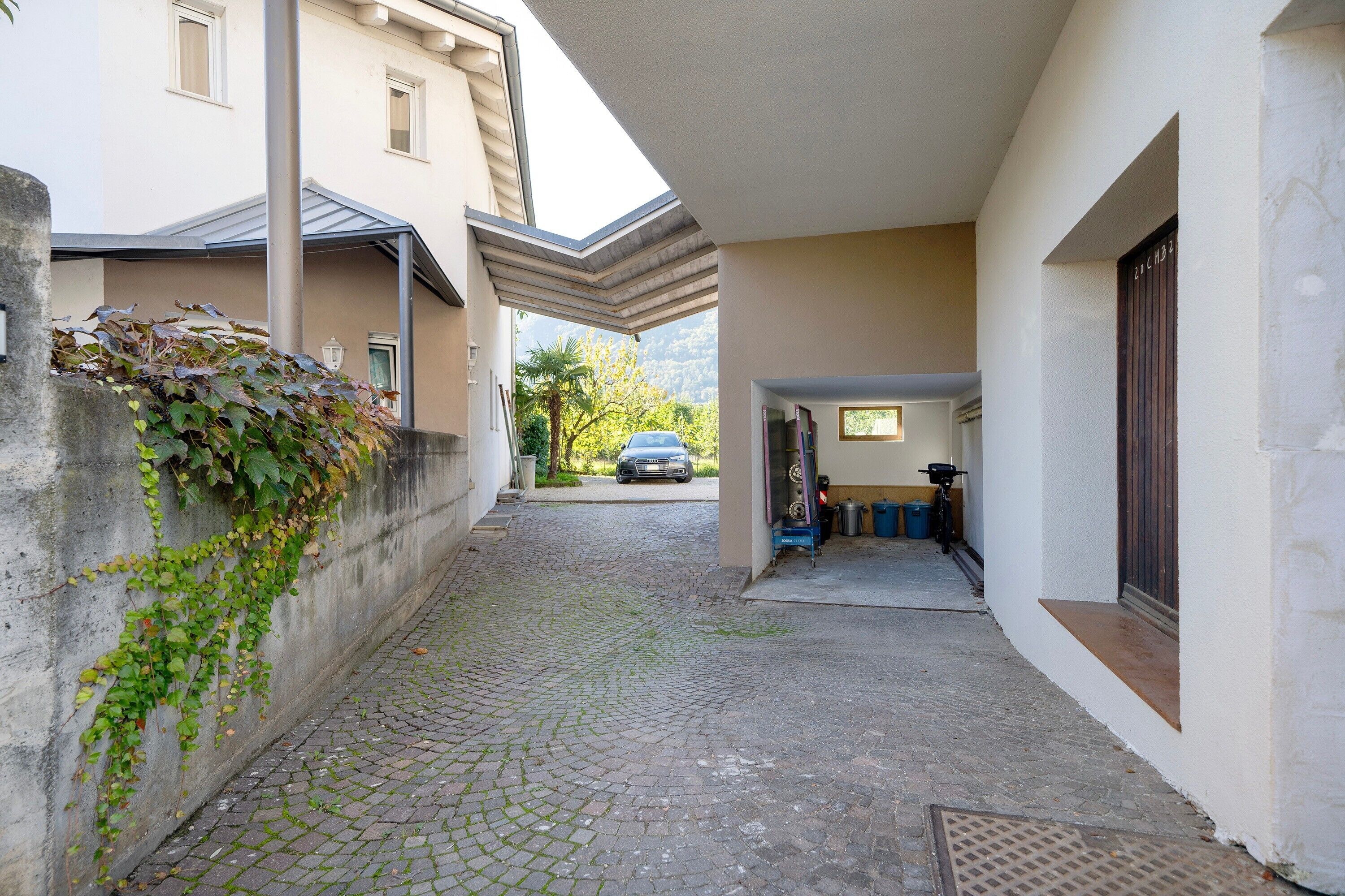 A narrow cobblestone alleyway with a building on one side and a parked car in the distance.