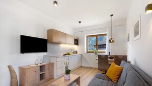 A modern living space with a flat-screen TV, wooden cabinets, a grey sofa, and a dining area with a table and chairs. - Apartment 'Fuchsberger  A' with Mountain View, Wi-Fi and Air Conditioning (Lana)