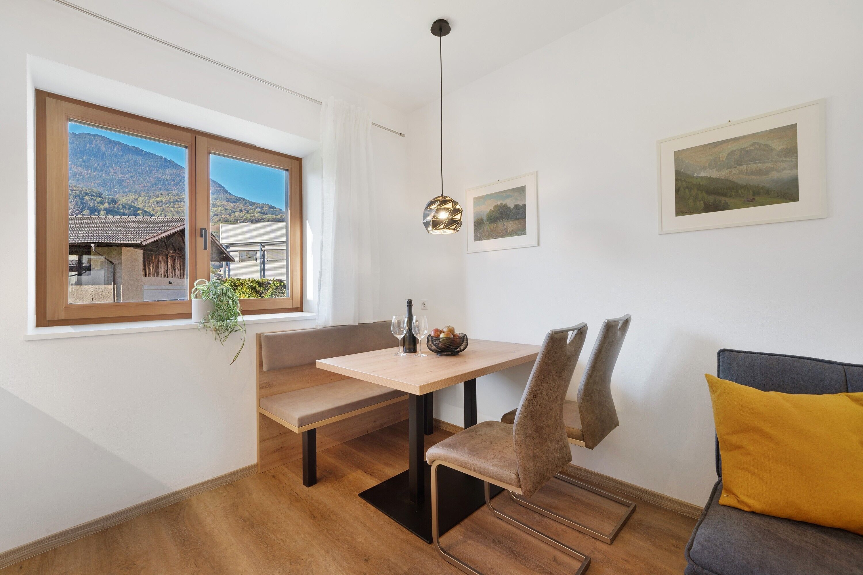 A dining area with a wooden table, bench, and chairs, a hanging pendant light, and a window with a mountain view.