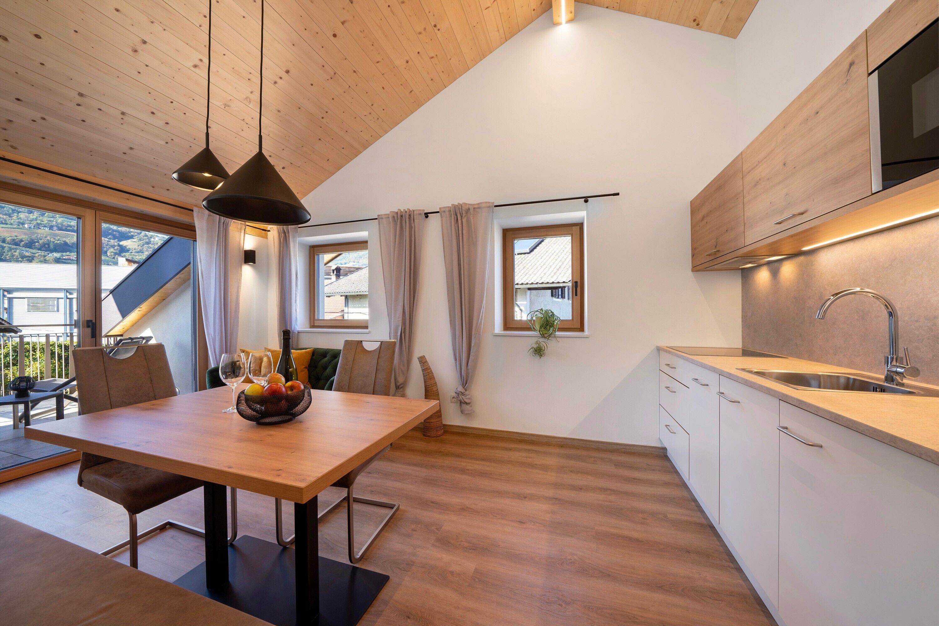 A modern kitchen with wooden cabinets, a dining area with a table and chairs, and a view of the outside.