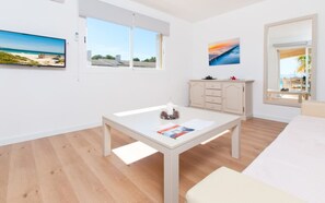 A modern room with a wooden floor, a white table with a magazine, a cabinet, and a bed.