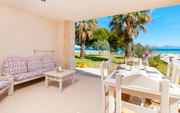 A balcony with a sofa and table, a view of the sea, and a dining area with chairs and a table.