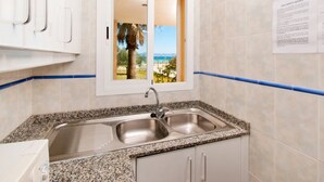 A kitchen with a double sink, granite countertop, and a window with a view of the beach.