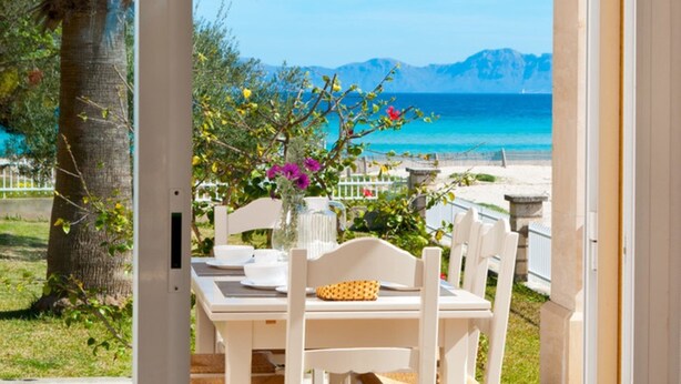 An outdoor dining area with a table and chairs, a vase with flowers, and a view of the sea and mountains.