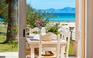 An outdoor dining area with a table and chairs, a vase with flowers, and a view of the sea and mountains.