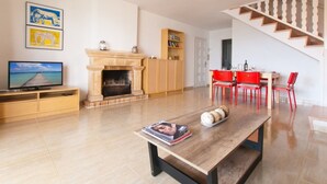 A living room with a fireplace, a television, a dining area with red chairs, and a staircase.