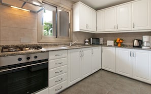 A modern kitchen with white cabinets, a gas stove, a microwave, and a coffee maker.