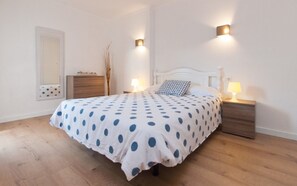 A bedroom with a bed, two bedside tables, a nightstand, a dresser, a mirror, and a wall-mounted light fixture.