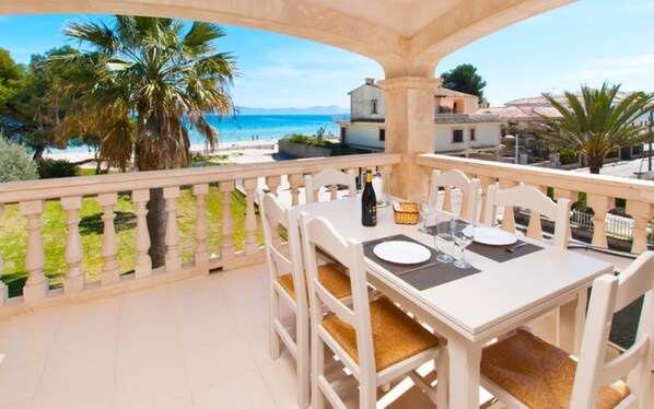 A balcony with a table set for two, overlooking a beach and ocean.