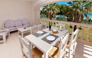 A balcony with a table set for two, a sofa, and a view of palm trees and the sea.