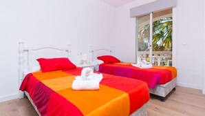 Ein Hotelzimmer mit zwei Betten, weißen Kopfteilen und einem großen Fenster mit Blick auf Palmen.