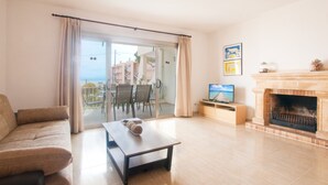Una sala de estar con sofá, mesa de centro, chimenea, televisor y balcón con vista a edificios y al mar.