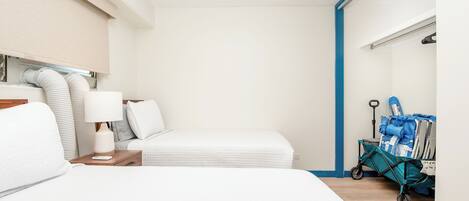 A hotel room with a bed, a nightstand, a lamp, a suitcase trolley, and a window with blinds.