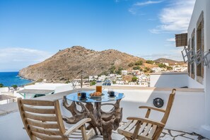 A terrace with a table and chairs, overlooking a coastal village and a mountain. - Room 'Double  Sea View No 1' with Sea View, Wi-Fi and Air Conditioning (Patmos)