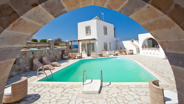 A pool area with a stone floor, lounge chairs, and a white building in the background. - Room 'Double  Sea View No 1' with Sea View, Wi-Fi and Air Conditioning (Patmos)