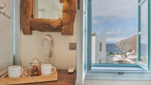 A room with a wooden tray holding cups and a jar, a mirror, and a view of a coastal town through a window. - Room 'Double  Sea View No 1' with Sea View, Wi-Fi and Air Conditioning (Patmos)