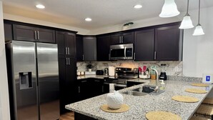 Una cocina moderna con armarios oscuros, electrodomésticos de acero inoxidable, encimeras de granito y una isla central con individuales tejidos.