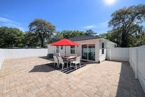 Une terrasse avec une table et des chaises, un parasol rouge et une clôture blanche.