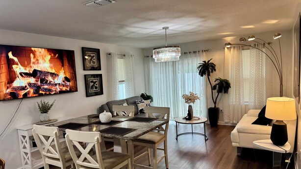 Una sala de estar moderna con comedor, que incluye una chimenea, un candelabro y un sofá blanco.