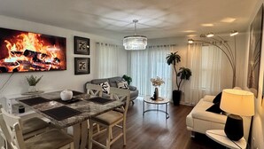Una sala moderna con una mesa de comedor, sofá y televisor mostrando una chimenea.