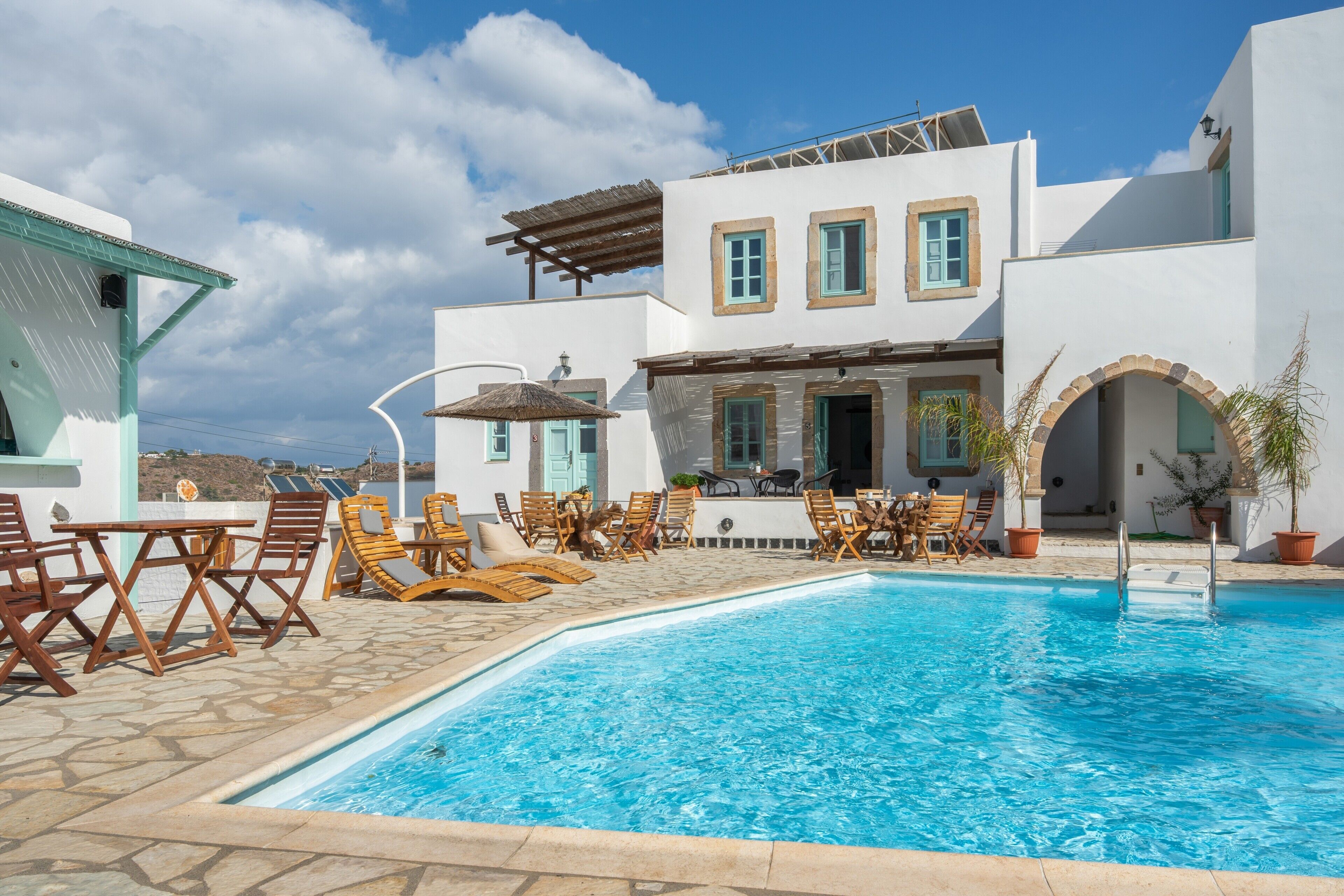 A poolside area with lounge chairs, a pool, and a building with a white facade and blue accents.