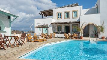 A poolside area with lounge chairs, a pool, and a building with a white facade and blue accents.